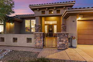 Exterior entry at dusk with a gate, stucco siding, stone siding, and a tile roof