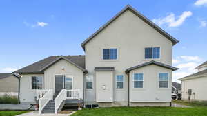 Back of house with stucco siding, a lawn, and a shingled roof
