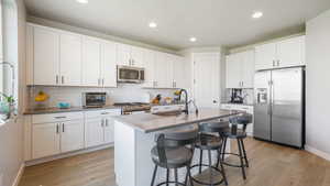 Kitchen with appliances with stainless steel finishes, tasteful backsplash, an island with sink, white cabinetry, and recessed lighting