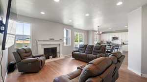 Living area featuring recessed lighting, light wood-style flooring, a chandelier, a textured ceiling, and a glass covered fireplace