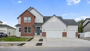 View of front facade with board and batten siding, driveway, a garage, a shingled roof, and brick siding