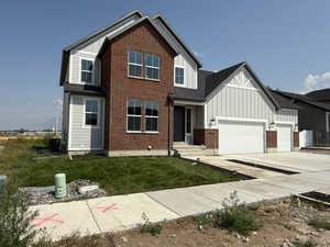 View of front of house with board and batten siding, concrete driveway, brick siding, a garage, and a front yard