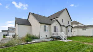 Rear view of house with a shingled roof, stucco siding, and a lawn
