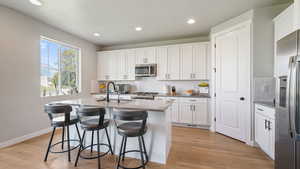Kitchen with decorative backsplash, appliances with stainless steel finishes, white cabinetry, a center island with sink, and recessed lighting