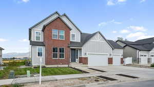 View of front of home featuring board and batten siding, concrete driveway, a mountain view, brick siding, and a front yard