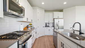 Kitchen with white cabinetry, appliances with stainless steel finishes, tasteful backsplash, light wood finished floors, and dark stone counters
