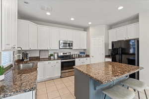Kitchen featuring appliances with stainless steel finishes, a kitchen bar, white cabinetry, recessed lighting, and a center island