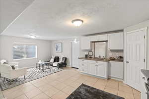Kitchen featuring light tile patterned floors, a textured ceiling, white cabinets, dark countertops, and open floor plan