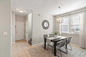 Dining space with light tile patterned flooring, a chandelier, and stairs