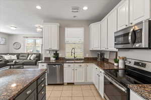 Kitchen featuring appliances with stainless steel finishes, white cabinetry, dark stone counters, light tile patterned flooring, and recessed lighting