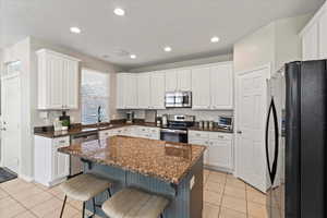 Kitchen with appliances with stainless steel finishes, white cabinets, light tile patterned flooring, a breakfast bar area, and recessed lighting