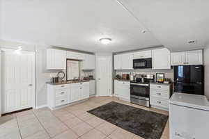 Kitchen featuring black appliances, light tile patterned floors, white cabinets, dark countertops, and a textured ceiling