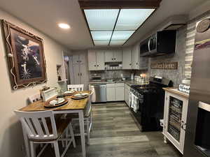Kitchen featuring backsplash, appliances with stainless steel finishes, white cabinets, dark wood finished floors, and recessed lighting