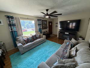 Living room featuring wood finished floors, a ceiling fan, and a textured ceiling