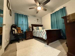 Bedroom featuring a textured ceiling, light colored carpet, and a ceiling fan
