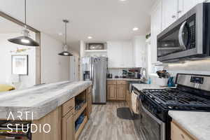 Kitchen with stainless steel appliances, decorative light fixtures, open shelves, decorative backsplash, and light wood-style flooring