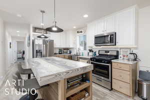 Kitchen with appliances with stainless steel finishes, white cabinets, pendant lighting, tasteful backsplash, and light wood finished floors