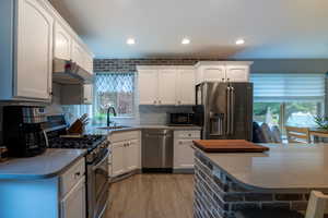 Kitchen with a breakfast bar area, stainless steel appliances, light wood-style flooring, white cabinets, and recessed lighting