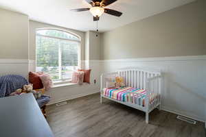 Bedroom with a wainscoted wall, wood finished floors, and a ceiling fan