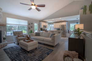 Living area featuring light wood-style flooring, ceiling fan, a fireplace, high vaulted ceiling, and recessed lighting