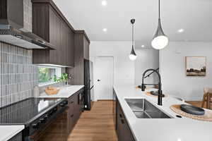 Kitchen with black appliances, wall chimney exhaust hood, light wood-style floors, modern cabinets, and dark brown cabinetry