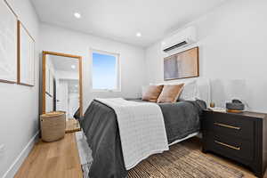 Bedroom with light wood-style floors, recessed lighting, and a wall unit AC