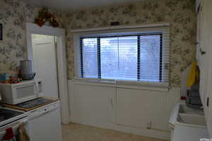 Kitchen with white appliances, wallpapered walls, a wainscoted wall, and light flooring