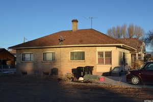 Back of property with brick siding, roof with shingles, and a chimney