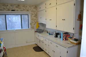 Kitchen with light countertops, light floors, wallpapered walls, white cabinets, and wainscoting