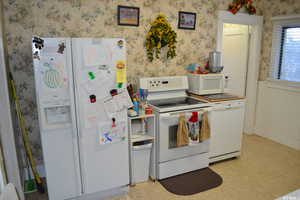 Kitchen featuring white appliances, wallpapered walls, and light floors