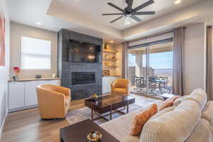 Living room featuring a raised ceiling, a fireplace, light wood-type flooring, healthy amount of natural light, and recessed lighting