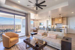 Living room featuring a tray ceiling, light wood-type flooring, recessed lighting, and ceiling fan