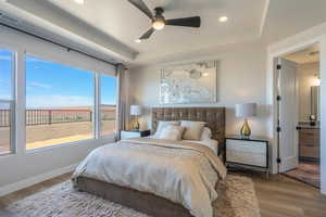 Bedroom with wood finished floors, a raised ceiling, recessed lighting, ceiling fan, and ensuite bath