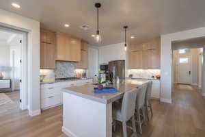 Kitchen featuring modern cabinets, light brown cabinetry, a breakfast bar, pendant lighting, and recessed lighting