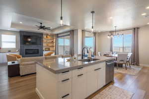 Kitchen featuring modern cabinets, white cabinets, decorative light fixtures, a tiled fireplace, and light wood-type flooring