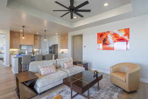 Living room featuring a tray ceiling, light wood-type flooring, recessed lighting, and a ceiling fan