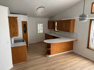 Kitchen featuring light countertops, a peninsula, light wood-type flooring, brown cabinetry, and vaulted ceiling