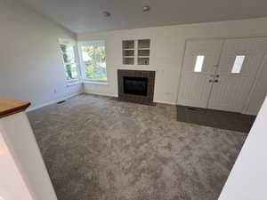 Unfurnished living room featuring dark colored carpet, a tiled fireplace, and lofted ceiling