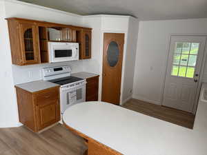 Kitchen with white appliances, light countertops, light wood-type flooring, and brown cabinetry