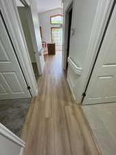 Corridor with light wood finished floors and vaulted ceiling