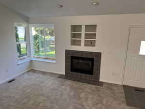 Unfurnished living room with a tile fireplace, carpet floors, built in features, and recessed lighting