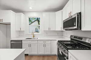 Kitchen with stainless steel appliances, white cabinetry, light wood-style flooring, and light stone counters