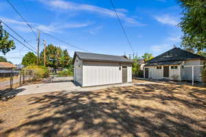 Back of property featuring an outdoor structure, a detached garage, and roof with shingles