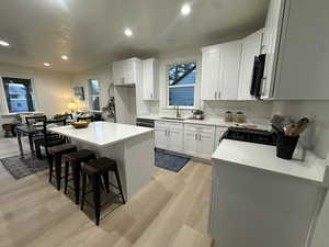 Kitchen with a kitchen bar, a kitchen island, white cabinets, gas range, and recessed lighting