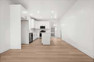 Kitchen with white cabinets, a center island, light countertops, light wood-type flooring, and stainless steel appliances