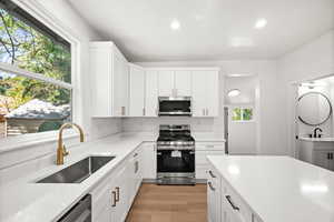Kitchen featuring appliances with stainless steel finishes, white cabinetry, light wood-style flooring, recessed lighting, and light stone counters