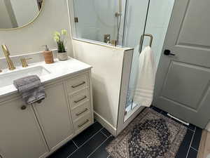 Full bath featuring a shower stall, vanity, and dark tile patterned flooring