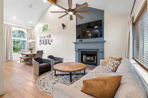 Living area featuring high vaulted ceiling, a fireplace, wood finished floors, a ceiling fan, and a chandelier