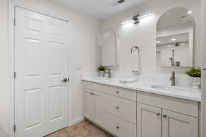 Bathroom featuring a tile shower, light tile patterned floors, and double vanity