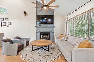 Living room featuring wood finished floors, a fireplace, high vaulted ceiling, and a ceiling fan